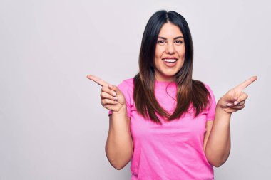 Genç, güzel, esmer, sıradan pembe tişörtler giyen, beyaz arka planda duran, kendine güvenen, parmakları farklı yönleri gösteren bir kadın. Reklam için boşluk kopyala