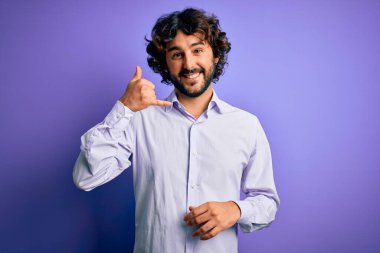 Mor arka plan üzerinde duran sakallı, genç ve yakışıklı bir iş adamı telefonda el ve parmaklarıyla telefonla konuşuyor gibi gülümsüyor. İletişim kavramları.