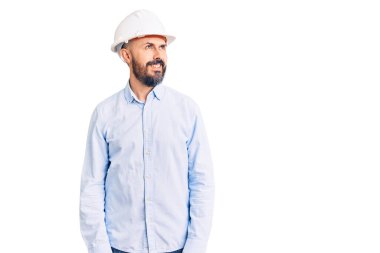 Mimar şapkası takan yakışıklı bir adam yüzünde gülümsemeyle yüzünü yana doğru çeviriyor, doğal bir ifade. Kendinden emin gülen. 