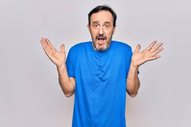 Orta yaşlı yakışıklı bir adam, sıradan tişörtler giyiyor. İzole edilmiş beyaz arka plan üzerinde duruyor. Hiçbir şeyden habersiz ve kolları açık, hiçbir fikri ve şüpheli bir yüzü var..