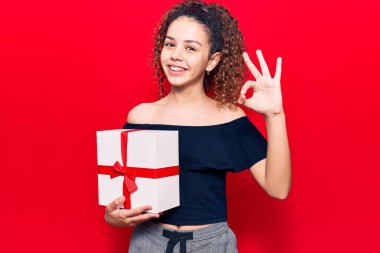 Kıvırcık saçlı güzel kız hediyesini tutuyor. Parmaklarıyla imza atıyor. Gülümsüyor. 