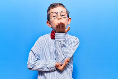 Sevimli sarışın, inek papyonu takan, gözlüklü ve kameraya bakıp havada öpüşen sevimli ve seksi bir çocuk. aşk ifadesi. 