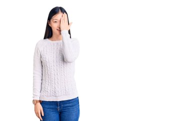 Genç, güzel, Çinli bir kadın gündelik süveter giyiyor. Bir gözünü eliyle kapatıyor. Yüzünde kendine güvenen bir gülümseme ve sürpriz bir duygu var.. 