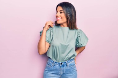 Genç ve güzel esmer kadın mutlu ve kendinden emin gülümsüyor. İzole edilmiş pembe arka planda yüzünde bir gülümsemeyle duruyorum.