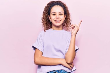 Kıvırcık saçlı güzel bir kız. Günlük kıyafetler giyiyor. Gülümsüyor. 