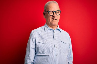 Orta yaşlı, yakışıklı, beyaz, sıradan çizgili tişört giyen, kırmızı arka planda gözlüklü, seksi bir ifadeyle kameraya bakan, neşeli ve mutlu yüzlü bir adam..