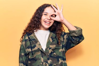 Kıvırcık saçlı, kamuflaj ceketli, mutlu gülümseyen güzel bir kız. 