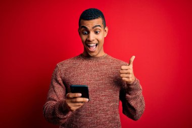 Yakışıklı Afrikalı Amerikalı adam kırmızı arka planda akıllı telefon kullanarak konuşuyor. Gururla bağırıyor, zaferi ve başarıyı kutluyor. Çok heyecanlı, coşkulu bir duygu.