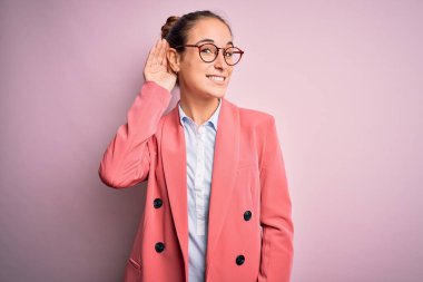 İzole edilmiş pembe arka planda ceket ve gözlük takan genç ve güzel bir iş kadını kulağına fısıldayarak dedikoduları ve dedikoduları dinliyor. Sağırlık kavramı.