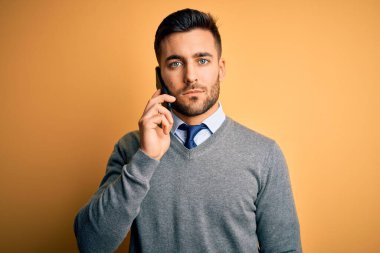 Genç yakışıklı bir adam akıllı telefondan konuşuyor sarı arka planda kendinden emin bir yüz ifadesiyle ciddi ciddi düşünüyor.