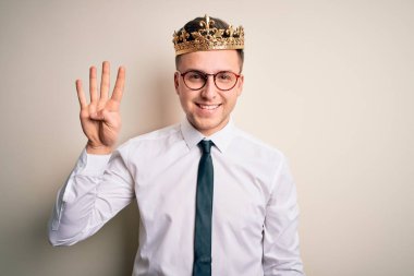 İzole edilmiş arka planda altın taç takan yakışıklı beyaz iş adamı kendini beğenmiş ve mutlu bir şekilde gülümserken dört numarayı işaret ediyor..