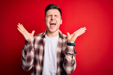 Kırmızı izole edilmiş arka plan üzerine gündelik modern tişört giyen yakışıklı beyaz adam kollarını kaldırmış ve gözleri kapalı heyecanla haykırarak başarının çılgınlığını kutluyor. Kazanan konsept