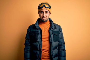 Kar giysileri ve kayak gözlüğü takan sakallı genç yakışıklı kayakçı üzgün ve endişeli, sinirli ve korkmuş. Üzücü ifade.