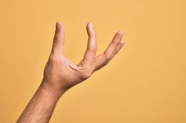 İzole edilmiş sarı arka plan üzerinde parmaklarını gösteren beyaz bir adamın eli. Görünmez bir şeyi alıp, parmaklarıyla uzayı gösteren bir nesneyi tutuyor.