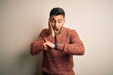 İzole edilmiş beyaz arka plan üzerinde duran sıradan bir süveter giyen genç, endişeli ve geç kalmaktan korkan bir adam.