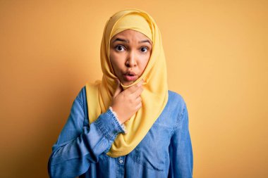 Kıvırcık saçlı, sarı arka planda geleneksel Arap başörtüsü takan genç ve güzel bir kadın elleri çenesinde olan inançsızlığa, şaşkınlığa ve hayrete düşmüş bir ifadeye hayran.
