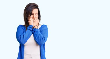 Gündelik kıyafetler giyen genç ve güzel bir kadın gergin görünüyor ve elleri ağızdan tırnak yiyor. anksiyete. 