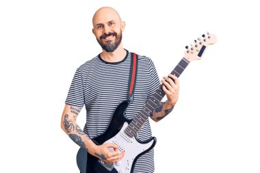 Genç yakışıklı adam elektro gitar çalıyor. Pozitif ve mutlu görünüyor. Kendine güvenen bir gülümsemeyle ayakta duruyor ve dişlerini gösteriyor. 