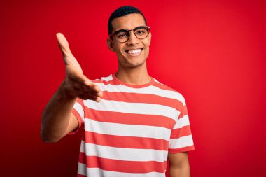 Genç, yakışıklı, Afro-Amerikalı bir adam, günlük çizgili tişört ve gözlük takıyor. Dostça bir selamlama ve hoş geldin hediyesi olarak gülümsüyor. Başarılı bir iş..