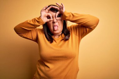 Güzel esmer ve cüsseli bir kadın izole edilmiş sarı arka plan üzerine gündelik süveter giyer. Dürbün gibi güzel hareketler yapar, gözler parmaklarından bakar. Çılgın ifade.