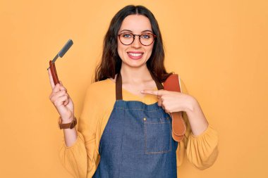 Önlük takan genç ve güzel bir berber kadın sarı arka planda jilet tutuyor.