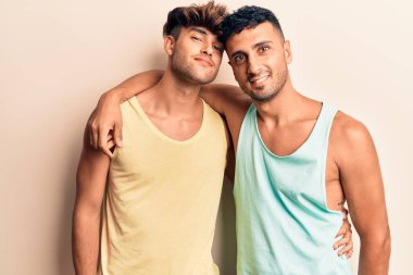 Yazlık kıyafetler giyen genç bir çift mutlu gülümsüyor. Yüzünde gülümsemeyle dikilip izole edilmiş beyaz arka planda sarılıyorum.