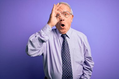 Gri saçlı, gözlüklü, gözlüklü, mor izole edilmiş arka planda duran yaşlı iş adamı şaşırmış yüz ifadesiyle şaşırmış, parmaklarından bakan bir jest yapıyor. İnançsız ifade.