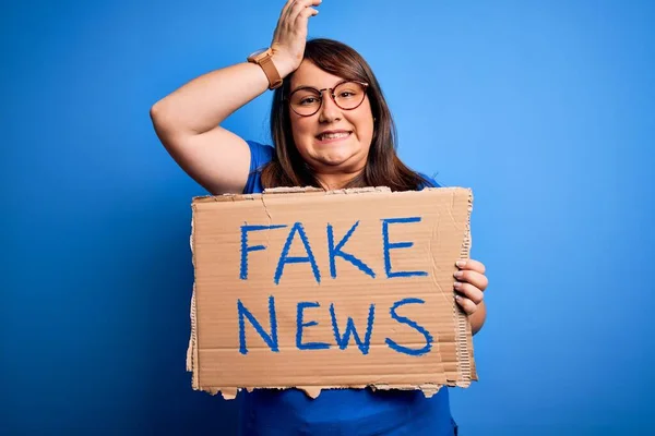 Beautiful plus size woman holding fake news banner for false journalism over isolated background stressed with hand on head, shocked with shame and surprise face, angry and frustrated. Fear and upset for mistake.
