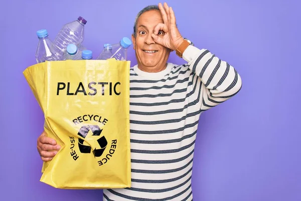 シニア男リサイクルバッグでプラスチックボトルでリサイクル幸せな顔で紫色の背景をリサイクルします — ストック写真