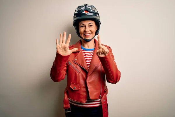 中年オートバイの女性身に着けていますオートバイヘルメットとジャケット上の白い背景表示と指差しますととともに指番号6ながら笑顔自信と幸せ — ストック写真