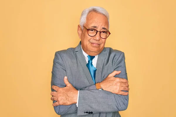 Middle age senior grey-haired handsome business man wearing glasses over yellow background shaking and freezing for winter cold with sad and shock expression on face