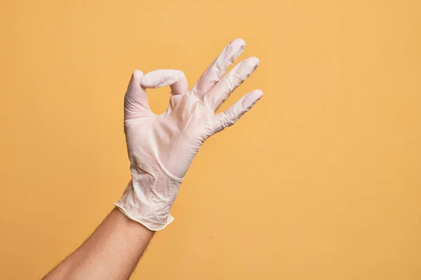 手里拿着医用手套的高加索年轻人的手 而不是孤立的黄色背景 表示赞许的表情 用手指做着不错的符号 — 图库照片