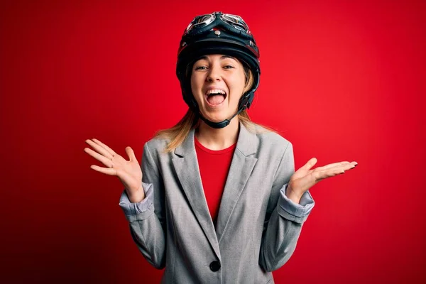 若い美しいブロンドのオートバイの女性は 赤い背景にオートバイのヘルメットをかぶって狂気を祝い 腕を上げ 興奮して叫んで目を開けて成功したことに驚いています 勝者のコンセプト — ストック写真