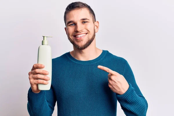 Joven Hombre Guapo Sosteniendo Botella Crema Sonriendo Feliz Señalando Con — Foto de Stock