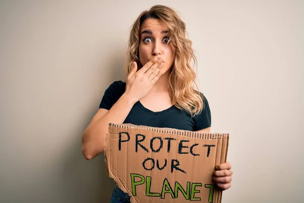 Young activist woman asking for environment holding banner with protect planet message cover mouth with hand shocked with shame for mistake, expression of fear, scared in silence, secret concept
