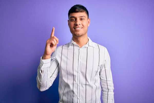 自信と幸せ笑顔ながら紫の背景に立っているエレガントなビジネスシャツを身に着けている若いハンサムなヒスパニック系の男 — ストック写真