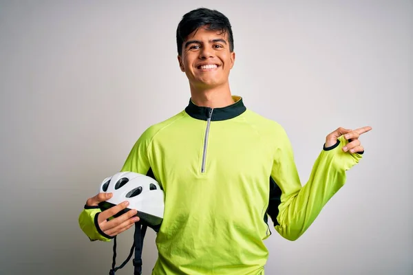 Young handsome cyclist man holding security bike helmet over isolated white background very happy pointing with hand and finger to the side