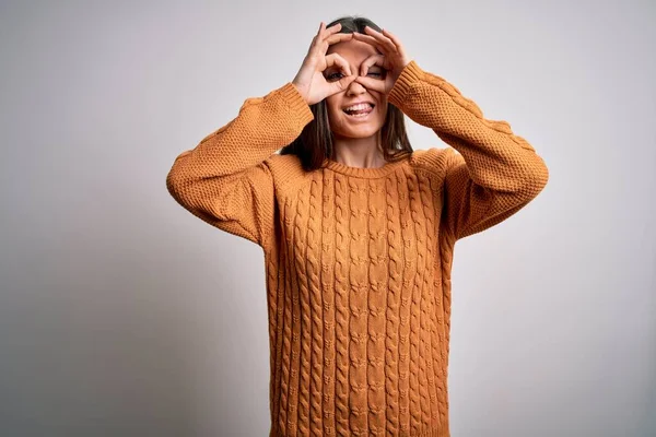 Young beautiful woman with blue eyes wearing casual sweater standing over white background doing ok gesture like binoculars sticking tongue out, eyes looking through fingers. Crazy expression.