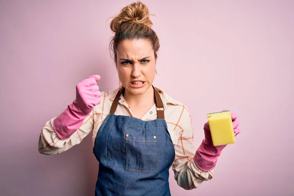 stock image Beautiful blonde cleaner woman doing housework wearing arpon and gloves using scourer annoyed and frustrated shouting with anger, crazy and yelling with raised hand, anger concept