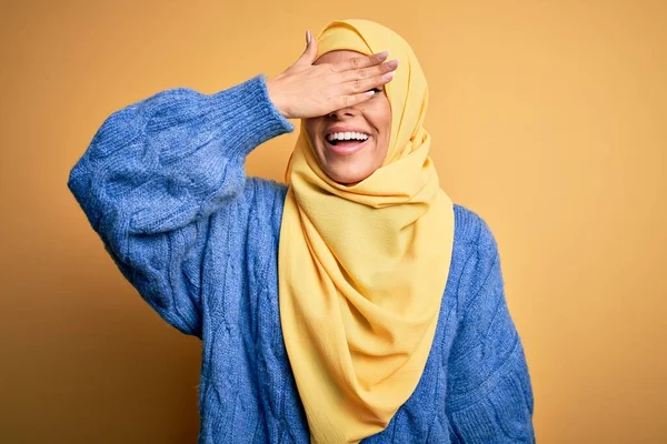 若い美しいブルネットのイスラム教徒の女性は 孤立した黄色の背景笑顔でアラブヒジャーブを身に着けており 驚きのために目をカバー顔に手で笑っています ブラインドコンセプト — ストック写真