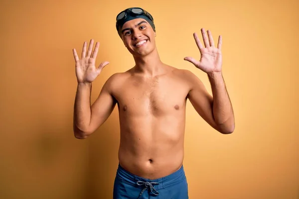 年轻英俊的男子穿着泳衣 戴着泳帽 披着孤立的黄色背景 露出十号手指 面带微笑 自信而快乐 — 图库照片