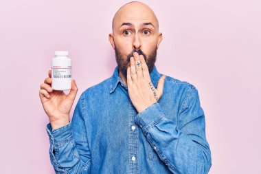 Genç ve yakışıklı bir adam elinde haplarla ağzını eliyle kapatıyor, şok geçiriyor ve hata yapmaktan korkuyor. şaşırmış ifade 