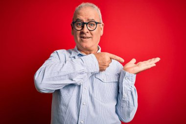 Orta yaşlı, beyaz, sıradan çizgili gömlek ve kırmızı arka planda gözlük takan yakışıklı adam kameraya hayret ediyor ve gülümsüyor..