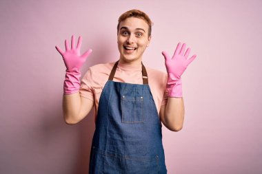 Genç, kızıl saçlı, önlük ve eldivenlerle ev işi yapan yakışıklı temizlikçi on numarayı gösterip gösterirken kendinden emin ve mutlu bir şekilde gülümsüyor..