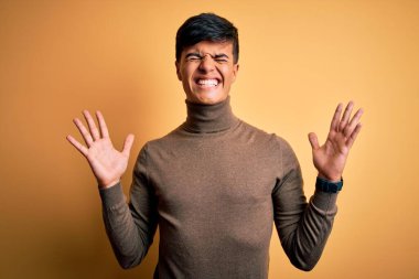 Sarı arka plan üzerine balıkçı yaka kazak giyen genç yakışıklı adam kollarını kaldırmış ve gözleri kapalı heyecanla haykırarak başarının çılgınlığını kutluyor. Kazanan konsept