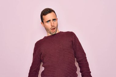 Mavi gözlü genç bir adam pembe arka planda sıradan bir süveter giyiyor. Şok olmuş bir yüz ifadesi var. Şüpheci ve alaycı görünüyor.