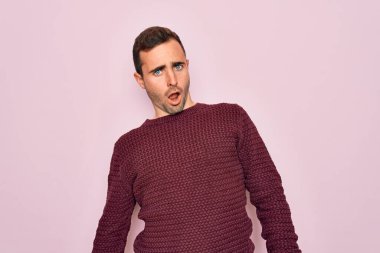 Young handsome man with blue eyes wearing casual sweater standing over pink background In shock face, looking skeptical and sarcastic, surprised with open mouth clipart