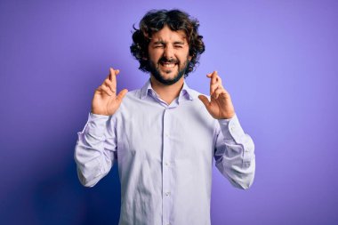 Mor arka plan üzerinde duran sakallı yakışıklı iş adamı umut ve gözler kapalı bir şekilde gülümseyerek işaret ediyor. Şans ve batıl inanç..