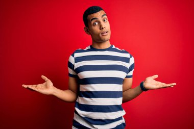 Yakışıklı Afro-Amerikan erkeği, sıradan çizgili tişört giyiyordu. Kırmızı arka planda duruyordu. Hiçbir şeyden haberi yoktu ve kolları açıktı..