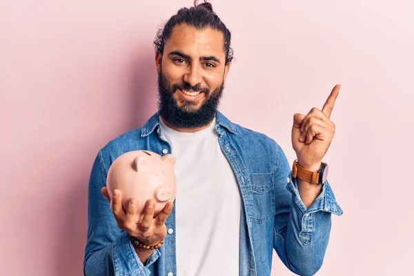 Fiatal Arab Férfi Kezében Malacka Bank Mosolygós Boldog Mutató Kézzel — Stock Fotó